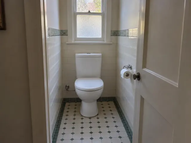 Clean white toilet in a narrow tiled bathroom with a frosted window in Strathfield