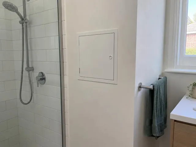 Neat access panel in a tiled bathroom wall beside a shower and window in Ashfield